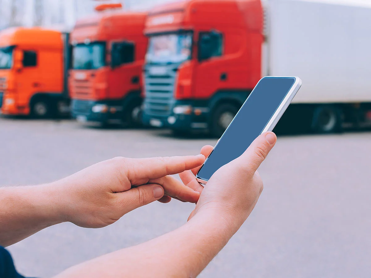 Persona usando un teléfono móvil frente a varios camiones de carga estacionados.
