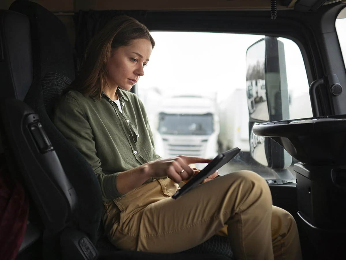 Mujer sentada en la cabina de un camión usando una tablet para revisar información.